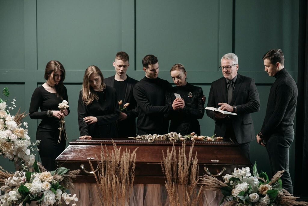 A funeral gathering with adults in a solemn indoor setting around a coffin, symbolizing loss and remembrance.