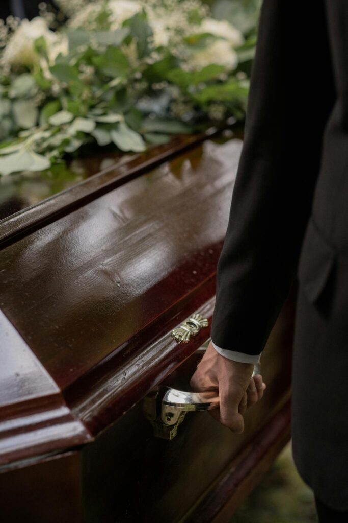 Close-up of a casket with a hand holding the handle during a funeral.